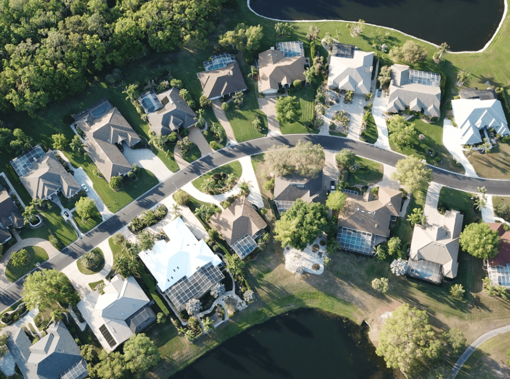 Aerial view of a luxurious residential community by Cornerstone Homes, featuring beautifully designed custom homes with pristine landscaping, private swimming pools, and nestled in a serene environment with a backdrop of a tranquil water body.